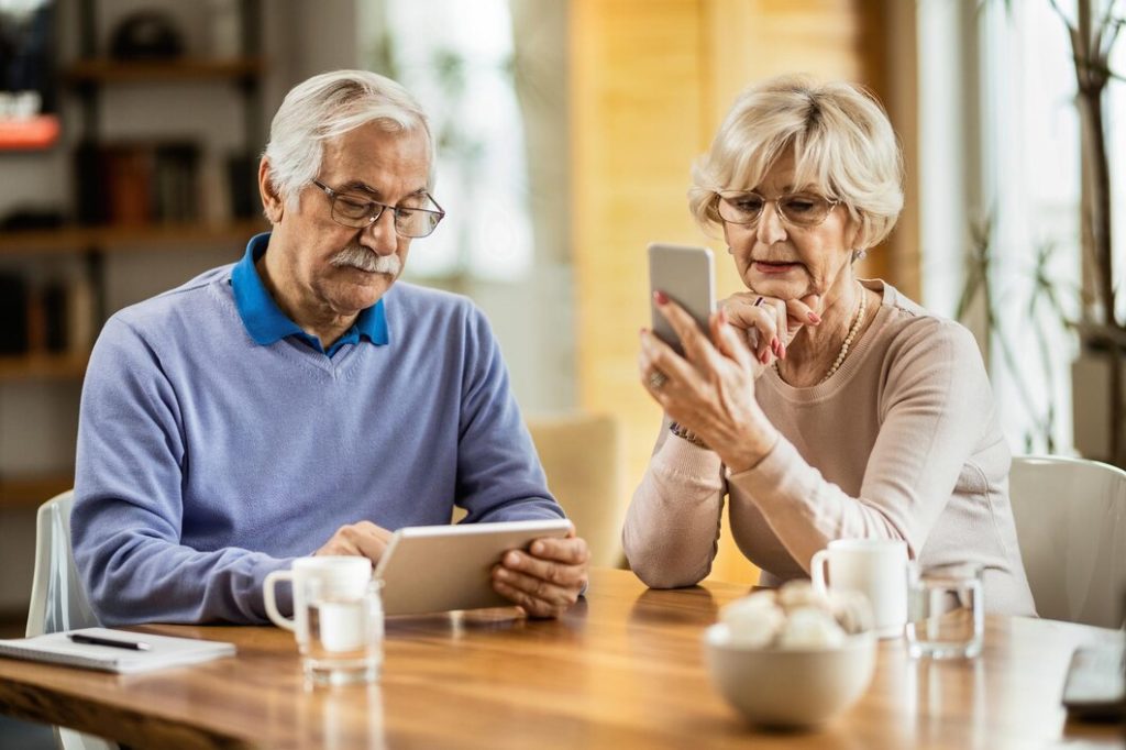 Image of a senior man surfing the internet on his tablet while his wife is text messaging on her mobile phone